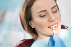 Dentist comparing color of woman teeth with dental implant