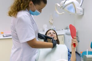 Mature woman patient choosing tooth implant looking at mirror in dental clinic.