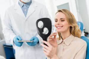 Woman choosing tooth implant looking at mirror in modern dental clinic