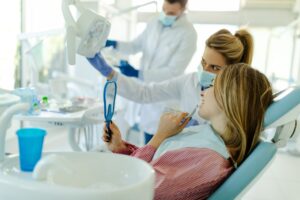 Young woman sitting in dental chair and selecting best color of implants using teeth samples.